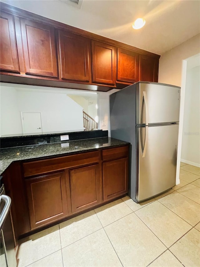 kitchen with dark stone countertops, light tile patterned floors, and stainless steel refrigerator