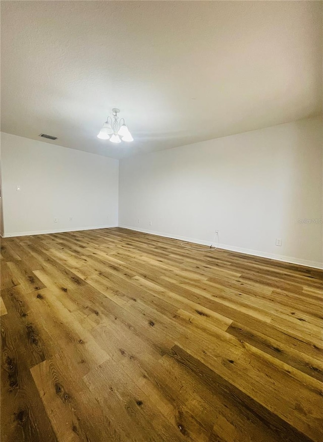 empty room featuring an inviting chandelier and light wood-type flooring