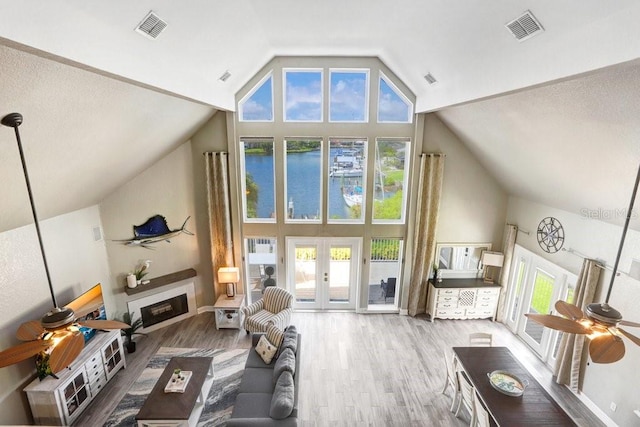 living room with hardwood / wood-style flooring, ceiling fan, a water view, high vaulted ceiling, and french doors