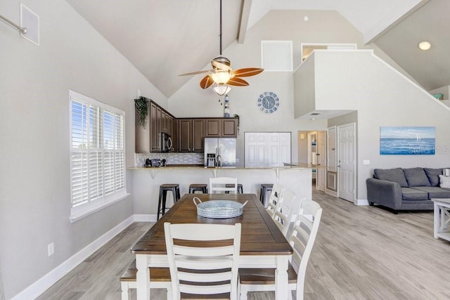 dining room featuring high vaulted ceiling, ceiling fan, light hardwood / wood-style floors, and beam ceiling