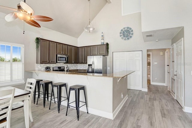 kitchen with a breakfast bar area, light hardwood / wood-style flooring, stainless steel appliances, decorative backsplash, and ceiling fan