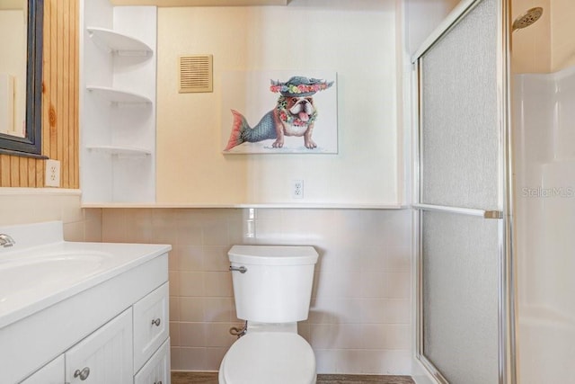 bathroom featuring vanity, walk in shower, toilet, and tile walls