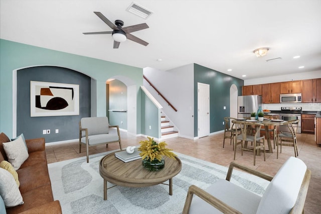 living room featuring light tile patterned floors, stairs, arched walkways, and visible vents