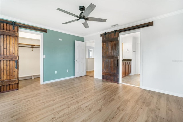 unfurnished bedroom with ornamental molding, ceiling fan, a closet, a barn door, and light hardwood / wood-style floors