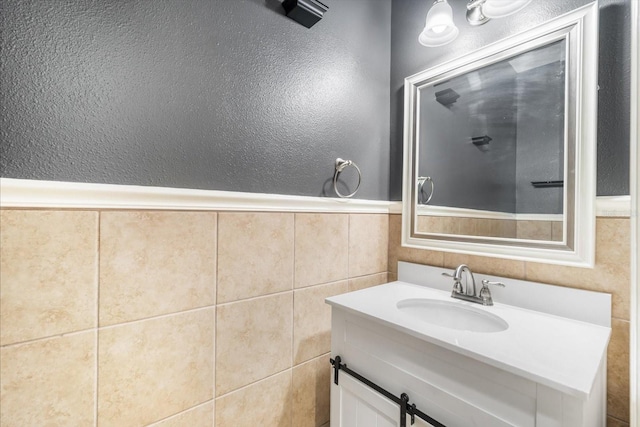 bathroom with tile walls, a wainscoted wall, a textured wall, and vanity