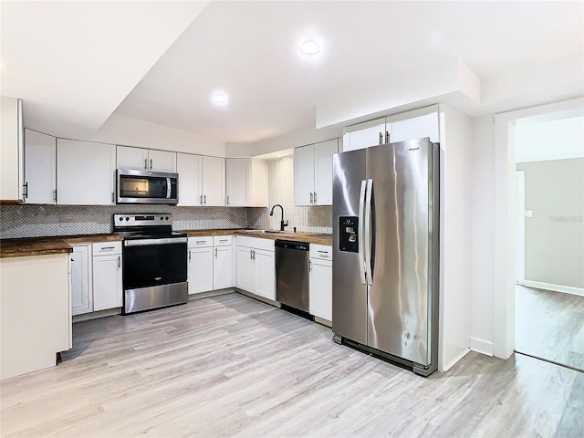 kitchen with white cabinets, stainless steel appliances, light hardwood / wood-style flooring, and tasteful backsplash