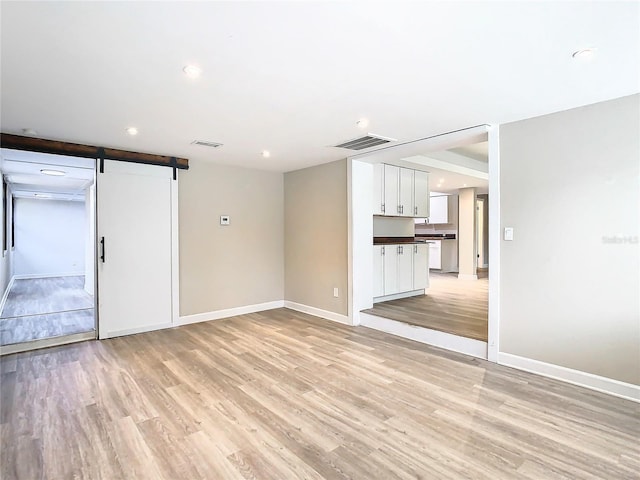 unfurnished living room with a barn door and light wood-type flooring