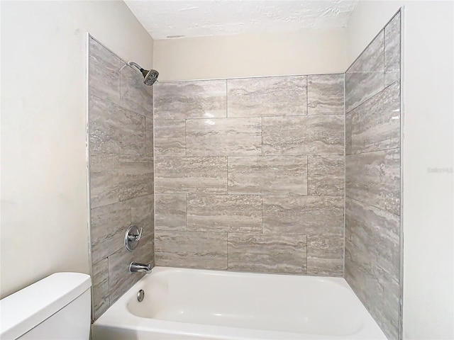 bathroom with toilet, a textured ceiling, and tiled shower / bath combo