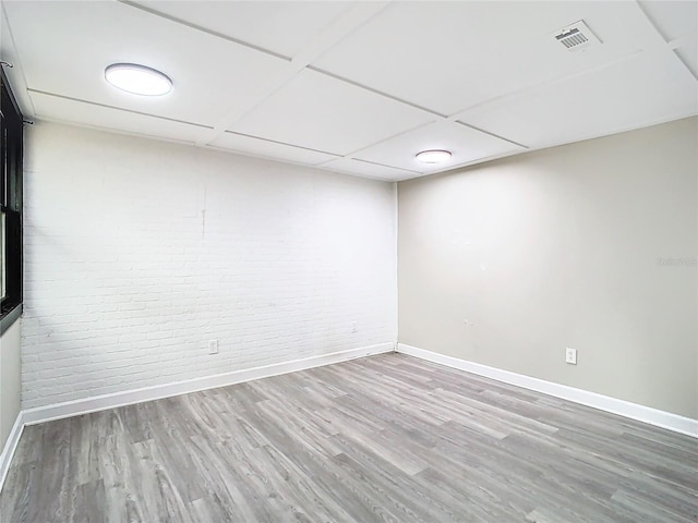 empty room featuring hardwood / wood-style flooring, a drop ceiling, and brick wall