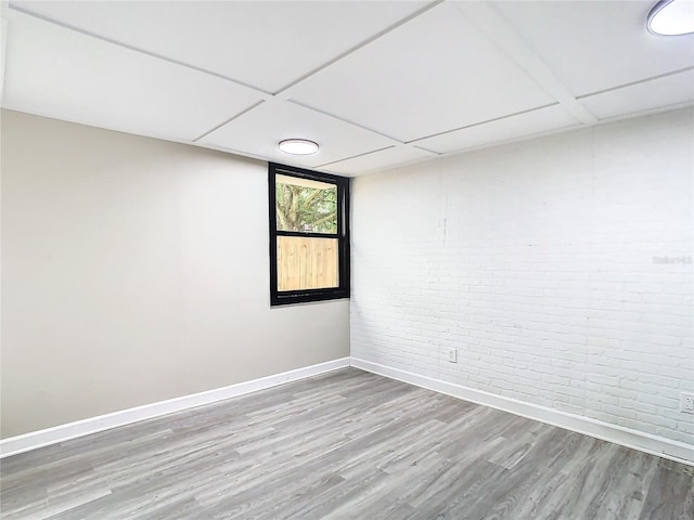 spare room featuring brick wall, hardwood / wood-style floors, and a drop ceiling