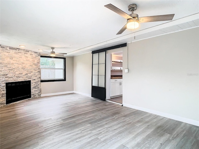 unfurnished living room with ceiling fan, hardwood / wood-style floors, and a stone fireplace