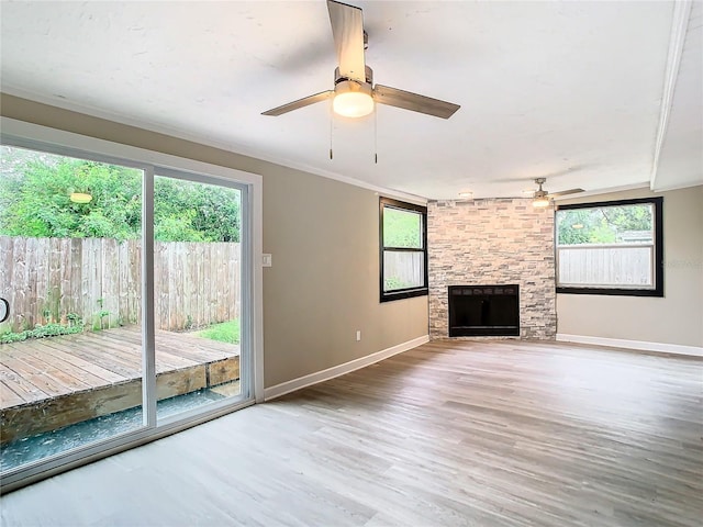 unfurnished living room featuring hardwood / wood-style flooring, a stone fireplace, ceiling fan, and ornamental molding