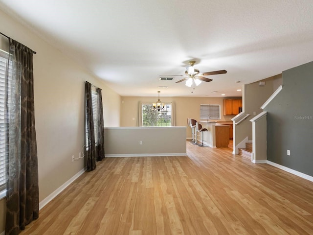 unfurnished living room featuring ceiling fan with notable chandelier and light hardwood / wood-style flooring