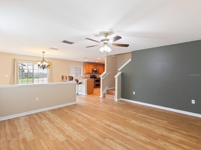 unfurnished living room featuring ceiling fan with notable chandelier and light hardwood / wood-style floors