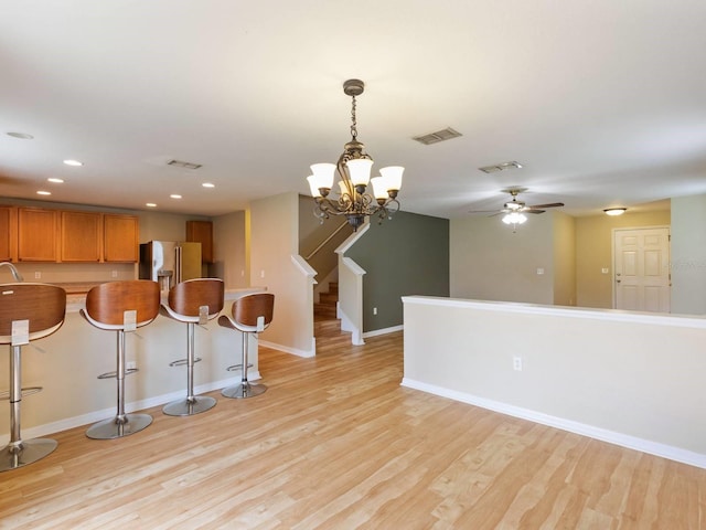 kitchen with high end refrigerator, a kitchen breakfast bar, pendant lighting, ceiling fan, and light hardwood / wood-style floors