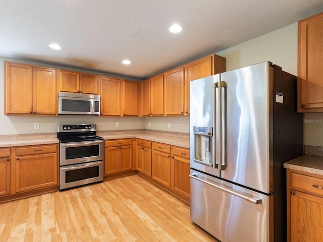 kitchen with appliances with stainless steel finishes, a textured ceiling, and light wood-type flooring