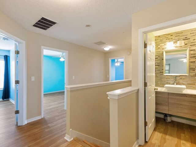 corridor with sink, light hardwood / wood-style flooring, and a textured ceiling