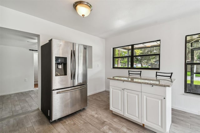 kitchen featuring white cabinetry, stainless steel fridge with ice dispenser, light stone counters, and light hardwood / wood-style floors