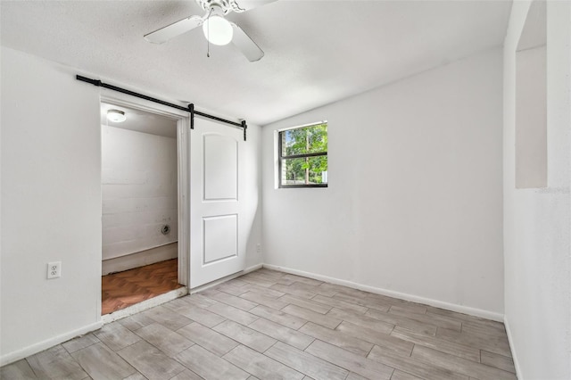 unfurnished bedroom featuring ceiling fan, a barn door, a textured ceiling, lofted ceiling, and light wood-type flooring