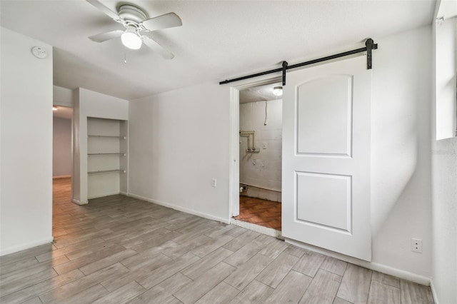 unfurnished bedroom with connected bathroom, a barn door, ceiling fan, and light wood-type flooring