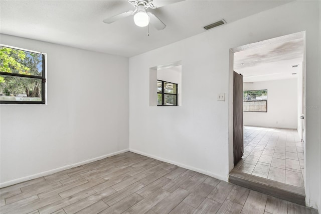 empty room featuring ceiling fan, a healthy amount of sunlight, light wood-type flooring, and a textured ceiling