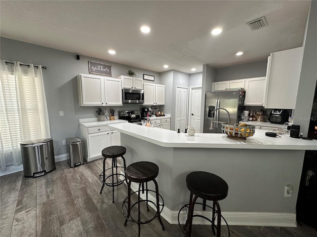 kitchen featuring kitchen peninsula, a breakfast bar, white cabinets, and appliances with stainless steel finishes