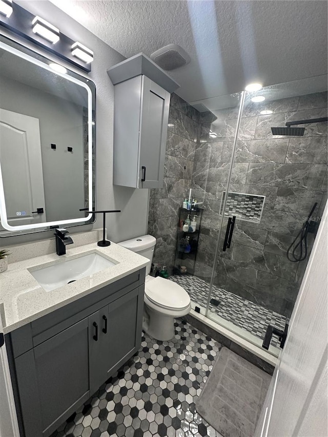 bathroom with vanity, toilet, a shower with door, and a textured ceiling