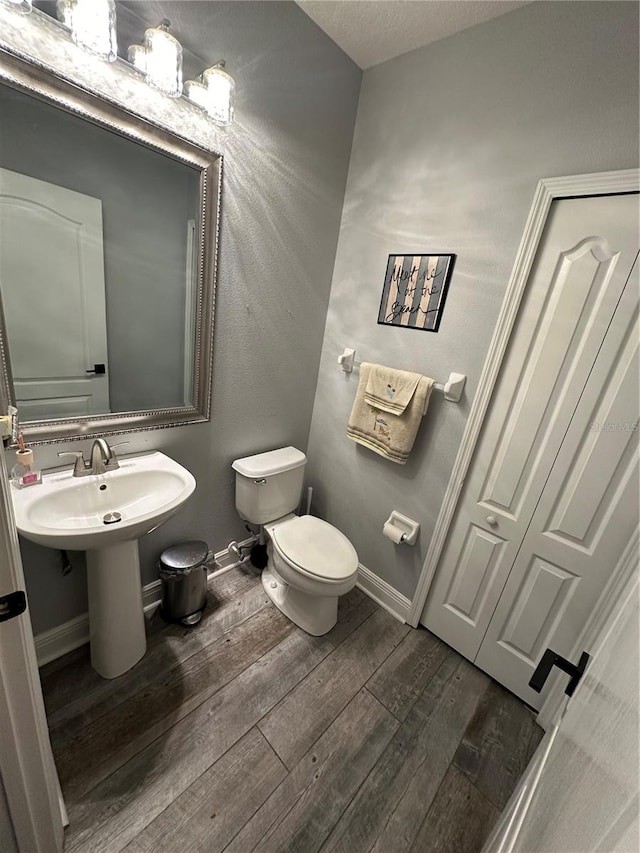 bathroom with wood-type flooring, toilet, sink, and a textured ceiling