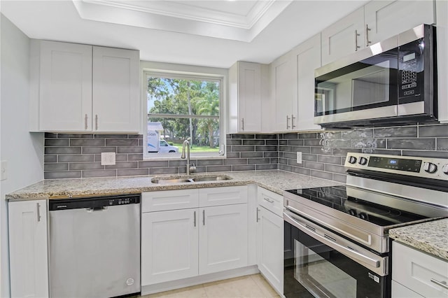 kitchen with appliances with stainless steel finishes, sink, tasteful backsplash, and a tray ceiling