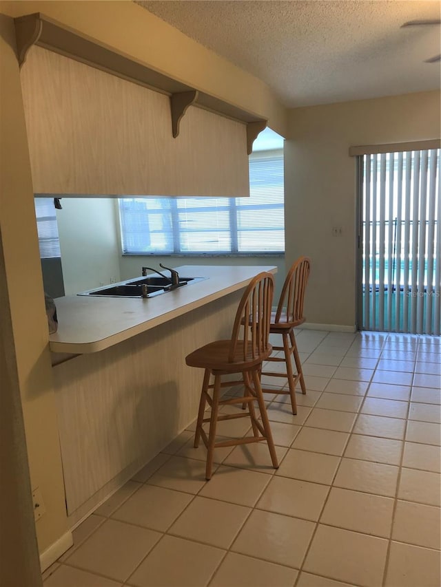 kitchen featuring light tile patterned flooring, a sink, light countertops, a textured ceiling, and a kitchen breakfast bar