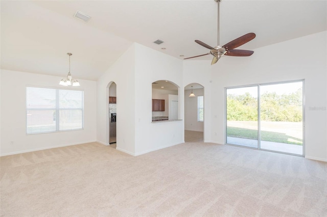 unfurnished living room with ceiling fan with notable chandelier, high vaulted ceiling, and light carpet