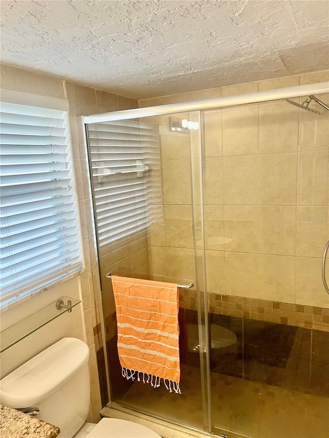 bathroom with a shower with door, a textured ceiling, and toilet