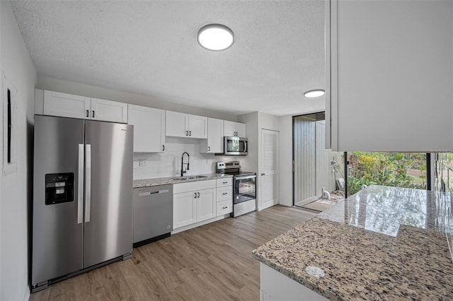 kitchen featuring white cabinets, light wood-style flooring, appliances with stainless steel finishes, light stone counters, and a sink