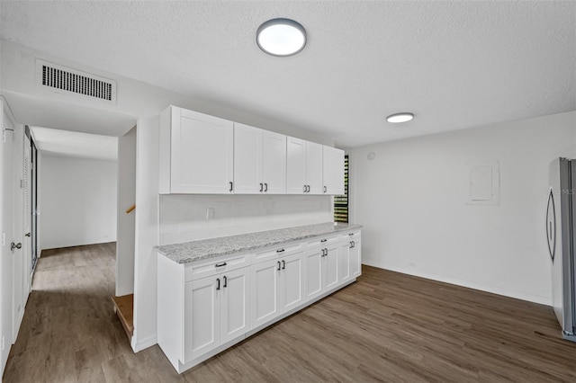 kitchen with light stone countertops, visible vents, white cabinets, and freestanding refrigerator