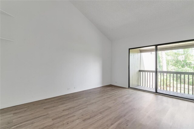 empty room with vaulted ceiling, a textured ceiling, and light wood-style flooring