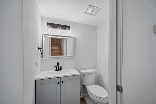 half bathroom featuring baseboards, visible vents, vanity, and toilet