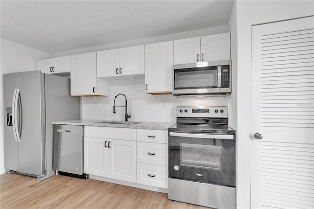 kitchen with backsplash, appliances with stainless steel finishes, white cabinets, a sink, and light wood-type flooring