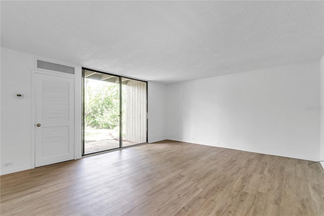 unfurnished room featuring a wall of windows, light wood-type flooring, visible vents, and a textured ceiling