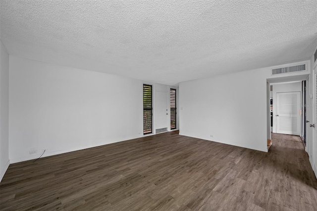 empty room featuring a textured ceiling, dark wood-style flooring, visible vents, and baseboards