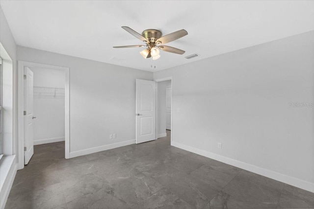 unfurnished bedroom featuring a closet, a spacious closet, ceiling fan, and dark tile patterned flooring