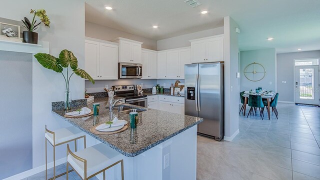 kitchen featuring stainless steel appliances, dark stone countertops, light tile patterned floors, and kitchen peninsula