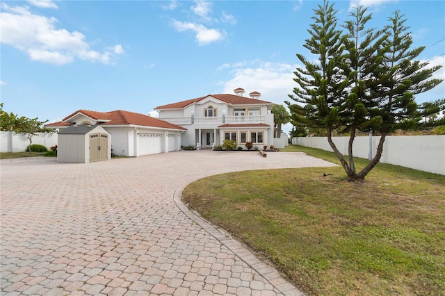 view of front of home with a storage unit, a balcony, a front lawn, and a garage