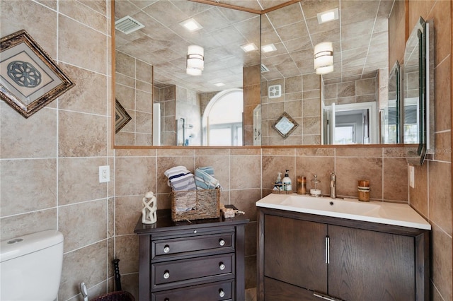 bathroom featuring vanity, toilet, and tile walls