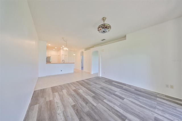 unfurnished living room featuring a chandelier and light hardwood / wood-style flooring