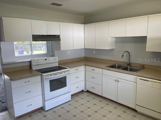 kitchen with white appliances, visible vents, a sink, under cabinet range hood, and white cabinetry