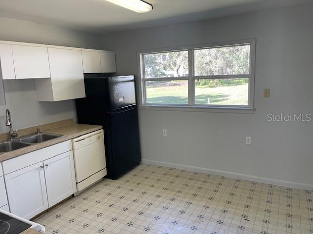 kitchen with a sink, light floors, dishwasher, and white cabinetry