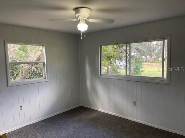 spare room with baseboards, a ceiling fan, and dark colored carpet