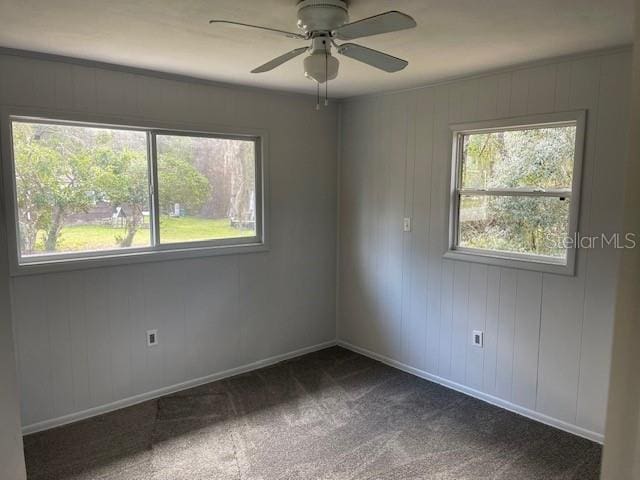 spare room with baseboards, dark colored carpet, and ceiling fan