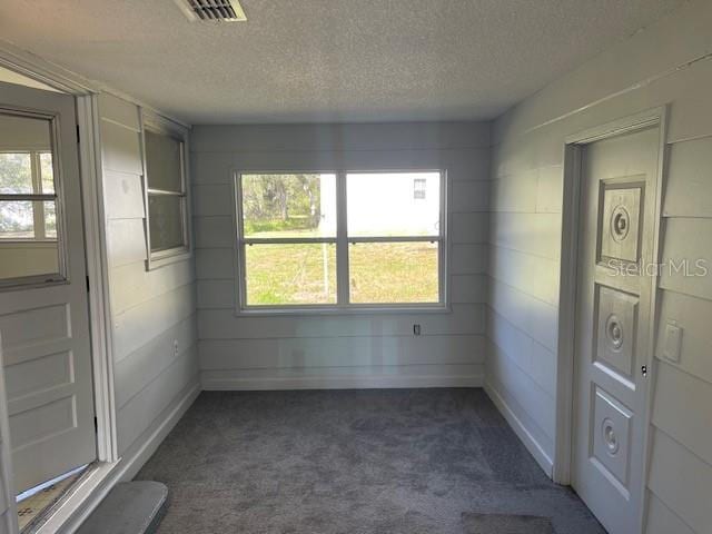 empty room with visible vents, dark carpet, and a textured ceiling