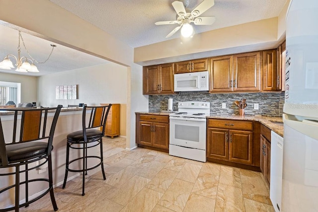 kitchen featuring ceiling fan with notable chandelier, white appliances, a textured ceiling, light tile patterned floors, and backsplash